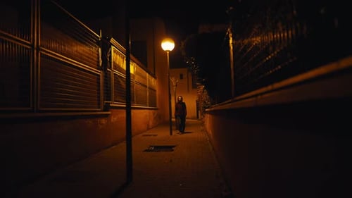 Narrow City Street in Darkness with Caucasian Woman Walking From Background and Leaving Wide Shot
