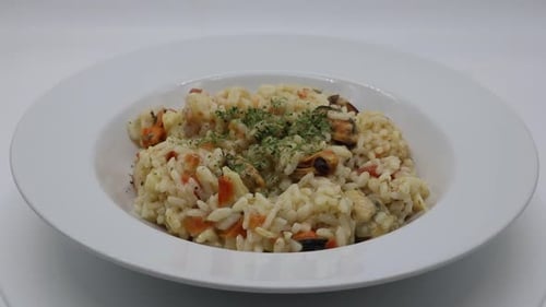 Risotto with seafood in a white dish rotating. Risotto ai frutti di mare, isolated on white backgrou