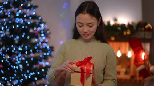 Slim Charming Asian Young Woman Standing in Living Room on Christmas Eve Opening Gift Box with