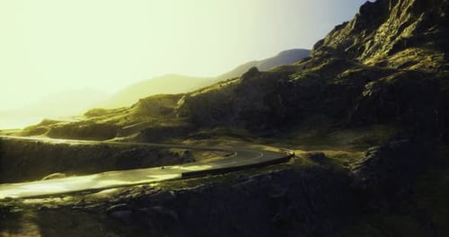 Winding Road Through Scenic Mountains During Golden Hour with Sunlight