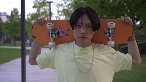 Handsome Asian Man with a Skateboard in the Park
