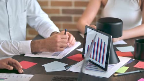 Three people are working and talking in the office. Gadgets and papers with graphs and information