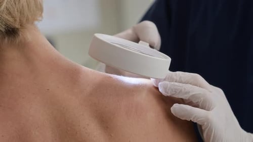 Mains d'un dermatologue examinant la peau des épaules à l'aide d'une loupe