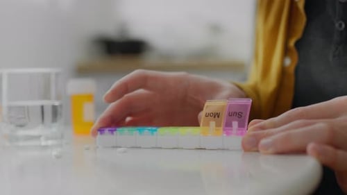 Organizer. A man suffering from a disease diligently puts pills into the cells of an organizer on