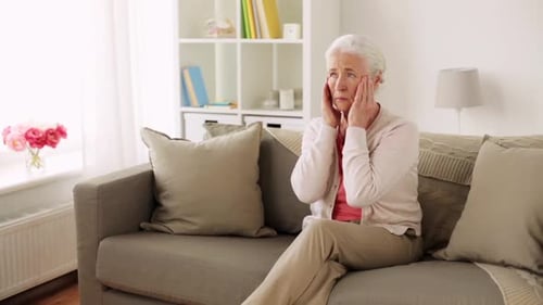 Senior Woman Massaging Temples Seated On Sofa