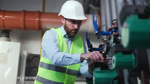 Plumber in Helmet Tightens Nut in Boiler Room Fixes Hot Water Pipe Service