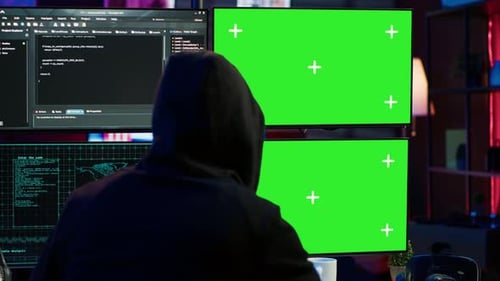 Gros plan d'un hacker exécutant du code dans un appartement sur des écrans de PC