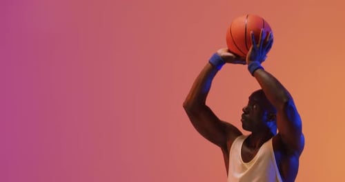 Video of african american male basketball player throwing ball on pink to orange background