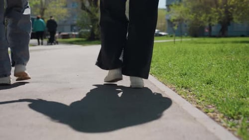 Two People Walking on Pavement Outdoors on a Sunny Day