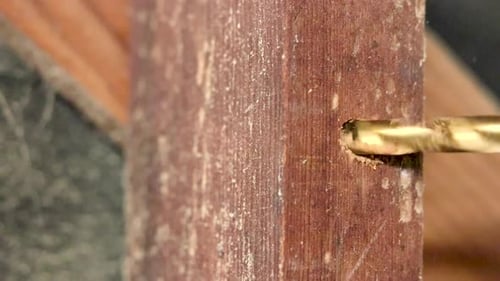 A SLOWMOTION close up shot of making a hole in a wooden block using a drill with a golden drill