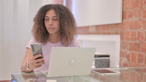 Young Woman Uses Phone and Laptop Indoors