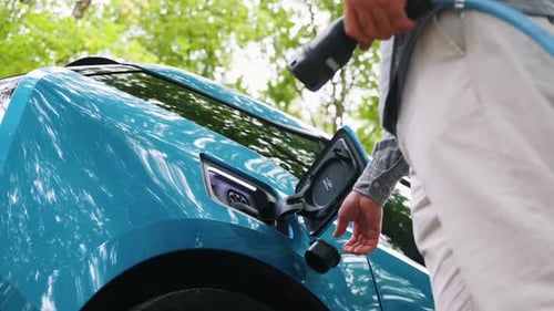 Young man charging electric car outdoor at green forest. Save ecology alternative energy sustainable