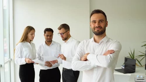 Smiling Mature Businessman Leader with Crossed Arms Looking at Camera Standing in Office at Team