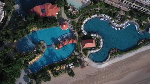 Resort swimming pool from top down aerial view on sunny morning including beach and beautiful landsc