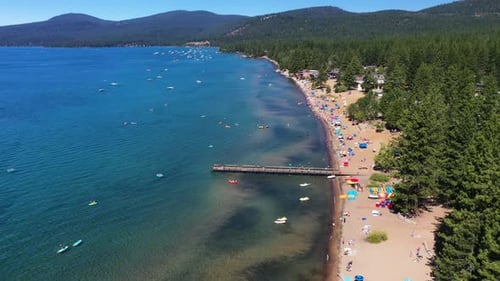 Aerial landscape view of people relaxing on a sandy lake beach surrounded by a pine forest in Lake T