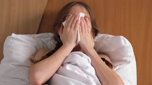 Sick Little Girl Sneezing and Blowing Her Nose Sitting on Bed at Home Close Up