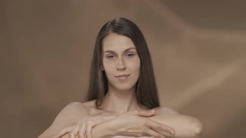 A Seminude Woman Enjoys the Velvety and Softness of the Skin of Her Hands in the Studio on a Brown