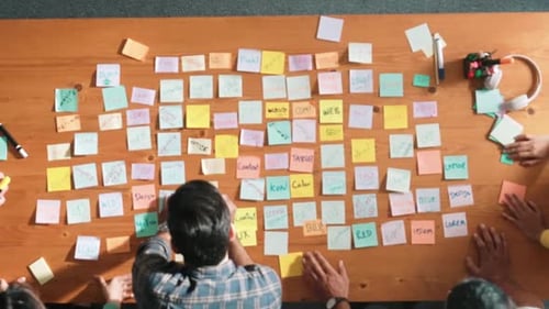 Top view of smart manager pointing at sticky note on meeting table. Symposium.