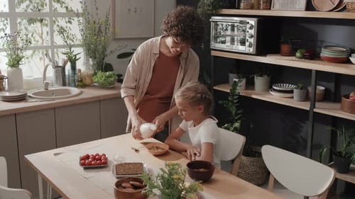 Mother Pours Milk for Child at Breakfast Table