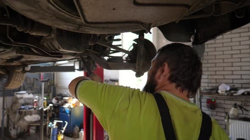 Male Auto Mechanic Works Underneath a Lifting Vehicle at Workshop Adult Professional Repairman