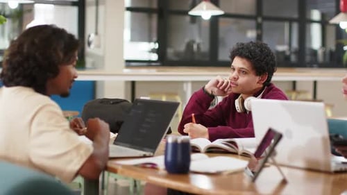 Étudiants afro-américains de sexe masculin à la table d'étude, penchés vers la gauche, tapant sur un ordinateur portable, clarifiant leurs devoirs
