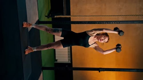 Vertical Video in a Sports Club on an Orange Background Redhaired Trainer Works with Two Dumbbells