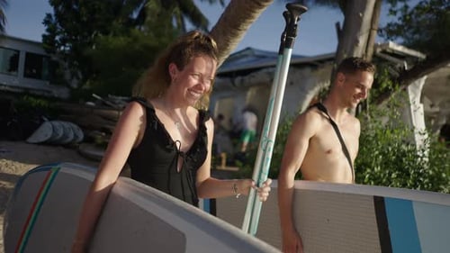 Couple Carry Paddleboards on Tropical Beach