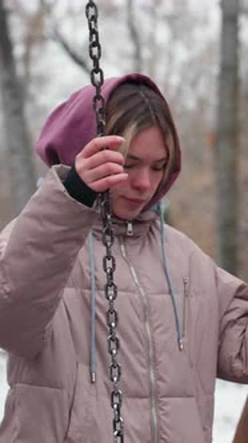 Young Lady Balancing on Iron Swing in Snowy Urban Park