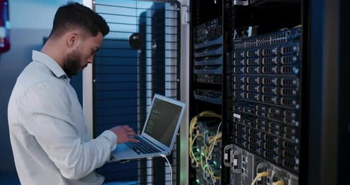Man Coding Next to Server Racks in Data Center