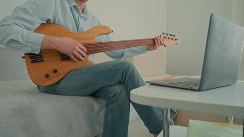 Man Plays Bass Guitar While Looking at Laptop