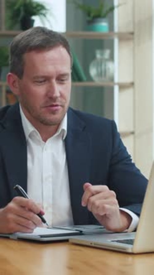 Man Taking Notes During Video Conference in Office