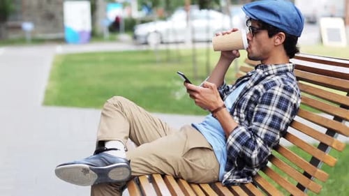 Hispanic man enjoying coffee and smartphone communication on a city street bench