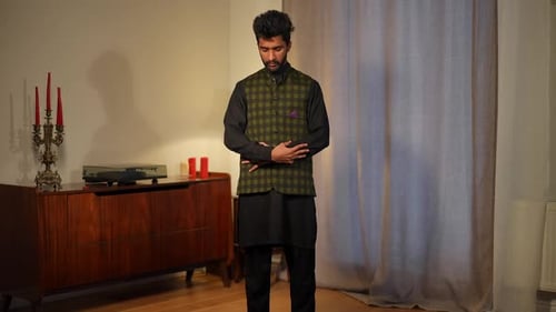 Weitwinkelaufnahme eines jungen muslimischen Mannes, der betet und sich auf einem Teppich im Wohnzimmer vor der Kamera verbeugt, Aufnahme von