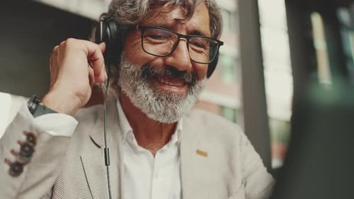 Clouse up, mature businessman and headphones, sits in an outdoor cafe and works using tablet