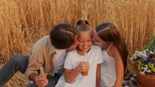 Family Enjoys Refreshments Together in Golden Wheat Field at Sunset