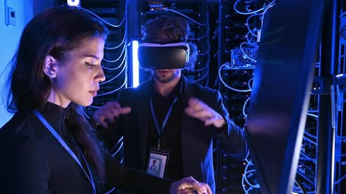Woman programming in a server room while a man is using a Virtual Reality headset