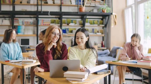 Portrait of Two Happy Female Multiracial Students Sit Attentively in the Foreground During a