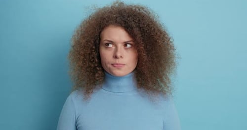 Thoughtful caucasian woman in blue turtleneck ponders a strange decision