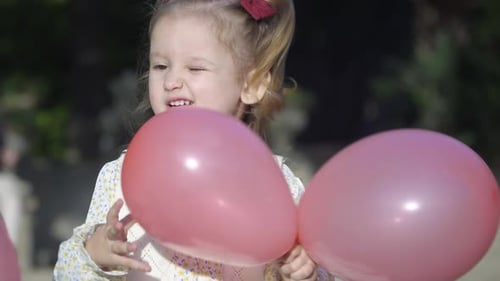 Close up of the cheerful little girl playing with the pink ballons in the park