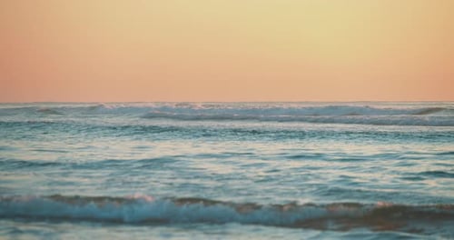 Wellen rollen am Strand heran und ein wärmender feurig-orangefarbener Sonnenuntergang.