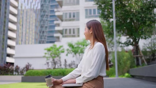 Asian young businesswoman holding a cup of coffee while sitting in city.