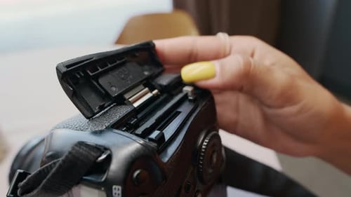 Mão feminina com unhas amarelas removendo o cartão de memória da câmera