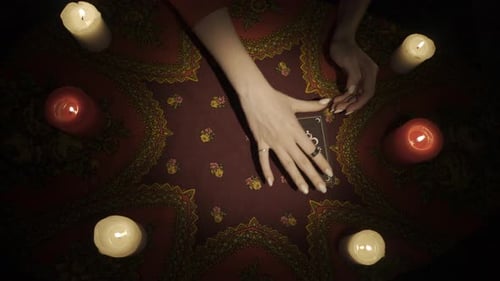 Vue de dessus : les mains d'une femme placent un éventail de cartes de tarot sur la table et ouvrent une carte montrant au