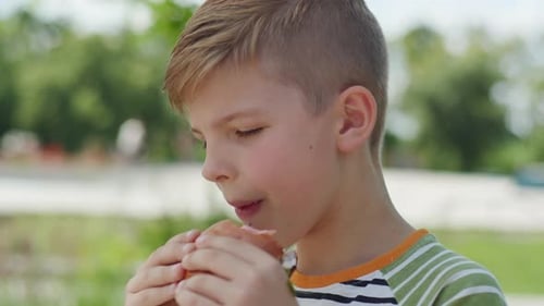 Boy Enjoys Burger Outdoors in Urban Park Close Up