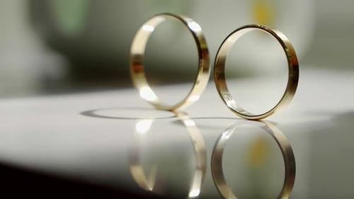 Close-up of golden wedding rings arranged on the surface of a glass table