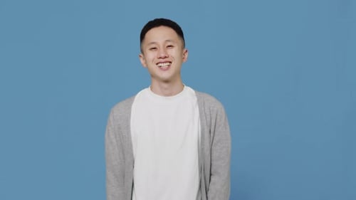 Ein junger, fröhlicher asiatischer Mann trägt ein strahlendes Lächeln, als er auf einem blauen Studiohintergrund steht. Konzept eines