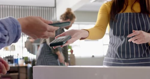 Midsection of caucasian female hairdresser and client paying with smartphone, in slow motion
