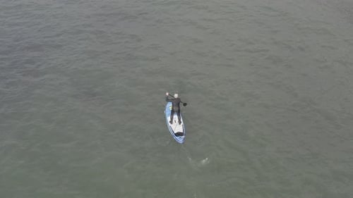 High angle aerial of wetsuit man on stand up paddleboard, choppy water