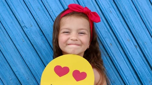 Adorable Girl Holds Smiling Face Emoji with Heart Eyes