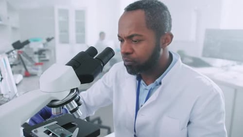 Close Up African American Scientist Man in Uniform Looking Under a Microscope Microbiologist Working